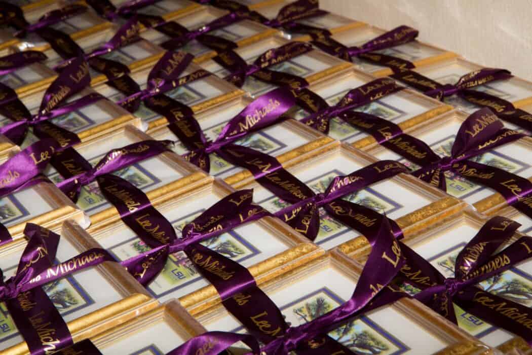 Rows of small framed pictures with gold borders, each tied with a purple ribbon printed with gold text.